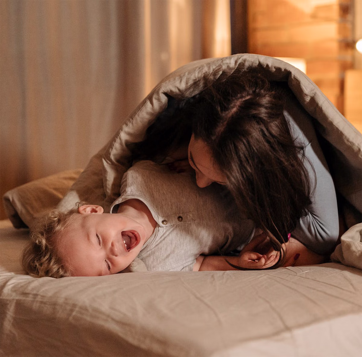 Madre e hijo jugando y riendo en la cama